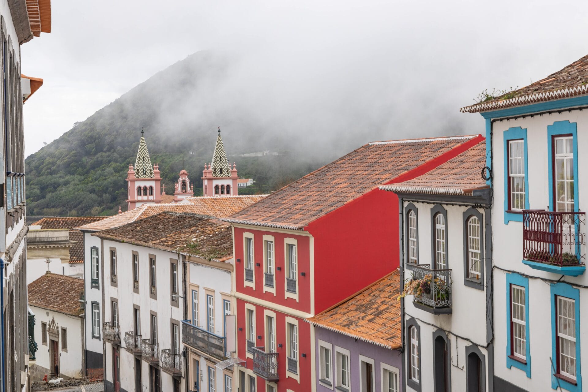 Colourful historic buildings and a distinctive pink and white church in the coastal town of Angra do Heroísmo on Terceira Island in the Azores with bright facades lining the street.